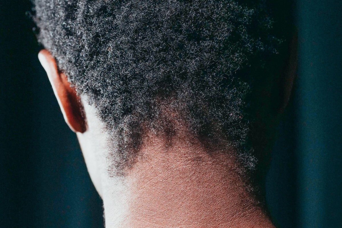 Nuque et cheveux crépus vus de dos en lumière naturelle, zone où la casse est fréquente