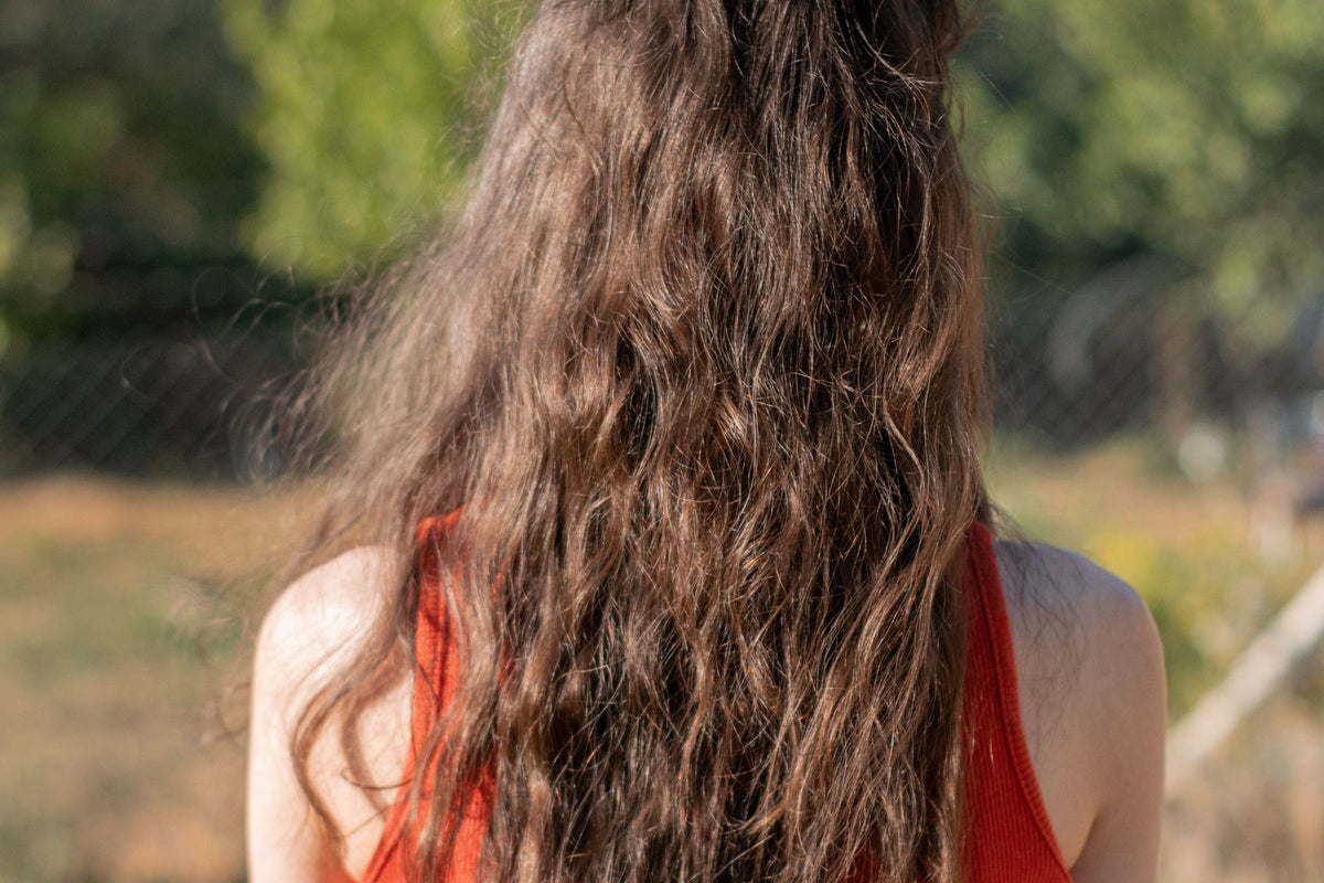 Femme de dos en débardeur orange, longs cheveux ondulés châtains au soleil