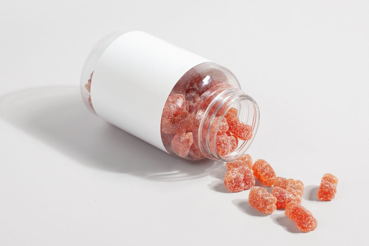 Pot de gummies renversé sur une table blanche, quelques gummies orangés éparpillés