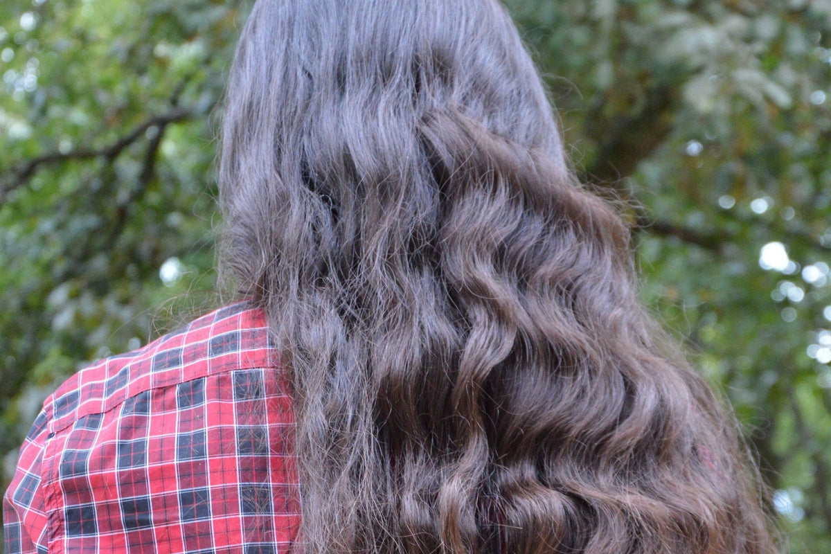 Vue de dos de longs cheveux ondulés châtains sur une chemise à carreaux rouge, en extérieur